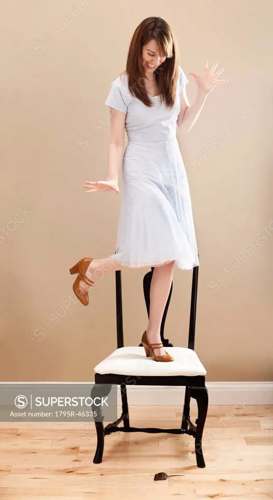 USA, Utah, Lehi, Young woman standing on chair, evading mouse