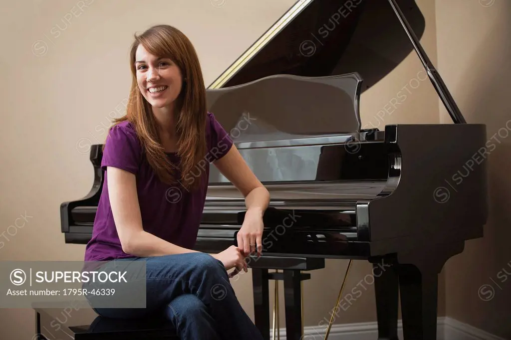 USA, Utah, Lehi, Young woman sitting by grand piano, smiling