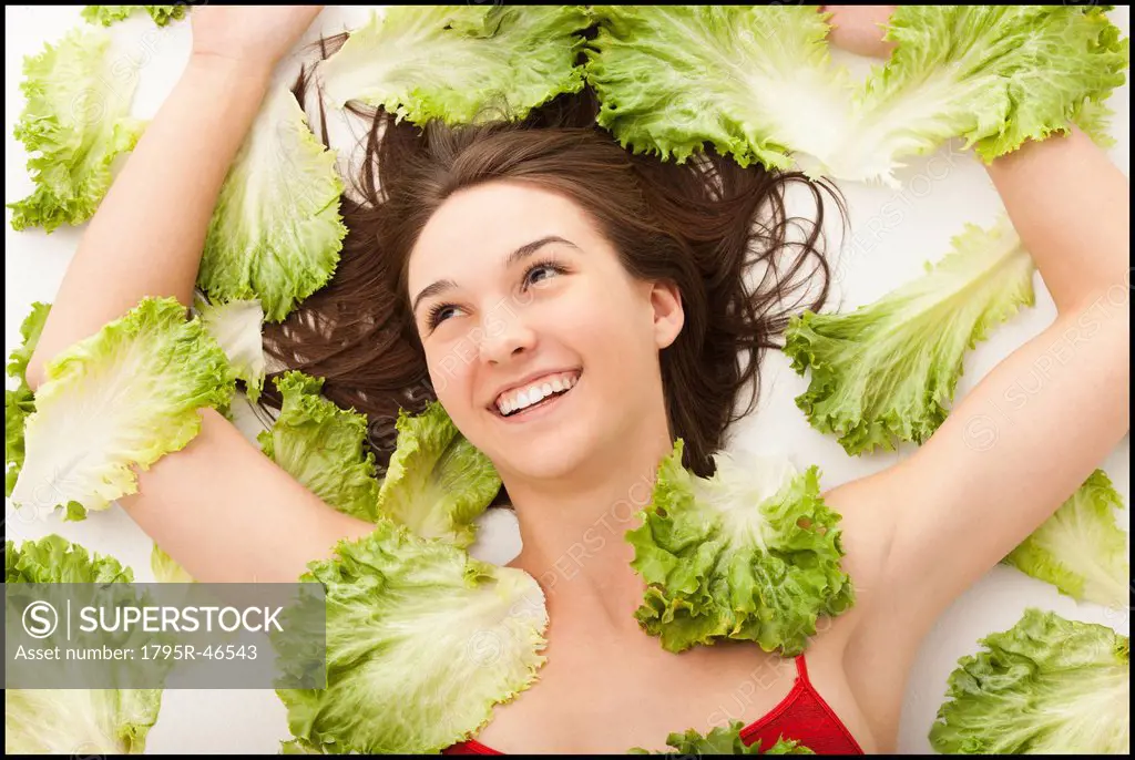 Young woman lying in lettuce leaves