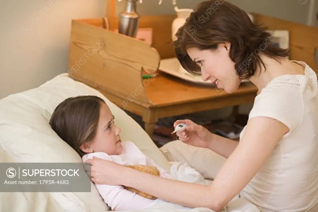 Mother checking young daughter s temperature with thermometer
