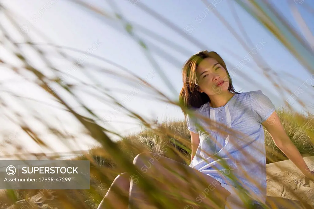 USA, California, Point Reyes, Young woman sitting in grass on sand dune