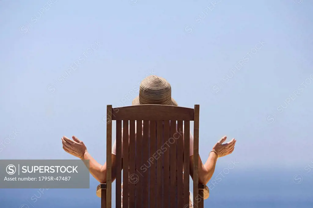 Spain, Costa Blanca, Rear view of woman sitting on wooden chair, facing sea