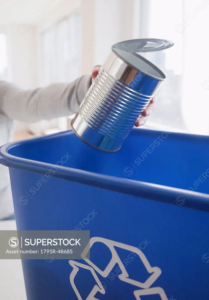 Woman putting metal can into blue recycling bin