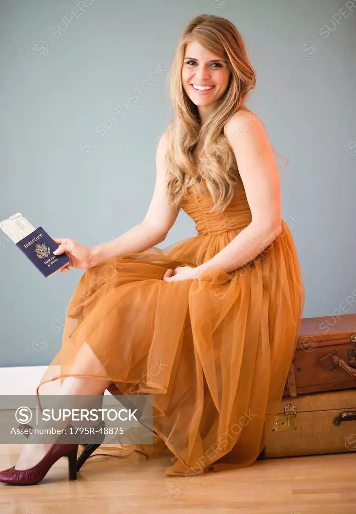 Woman in dress sitting on luggage and holding passport