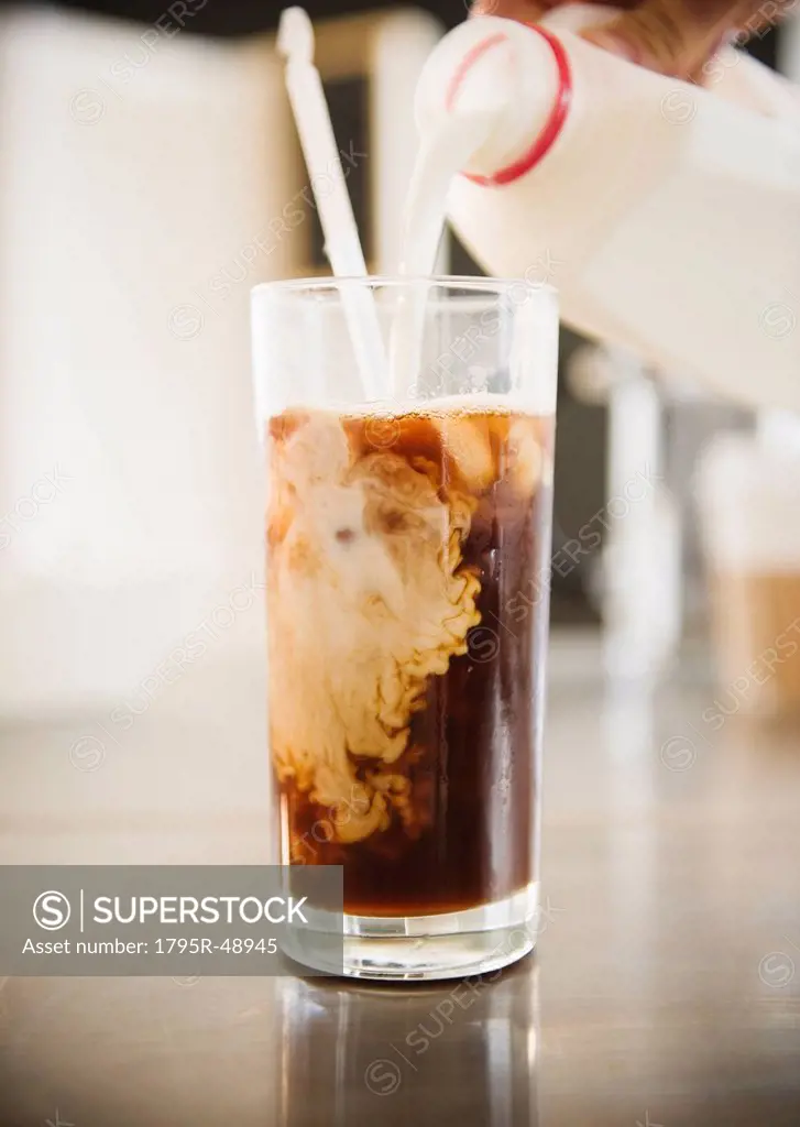Close up of hand pouring milk into iced coffee