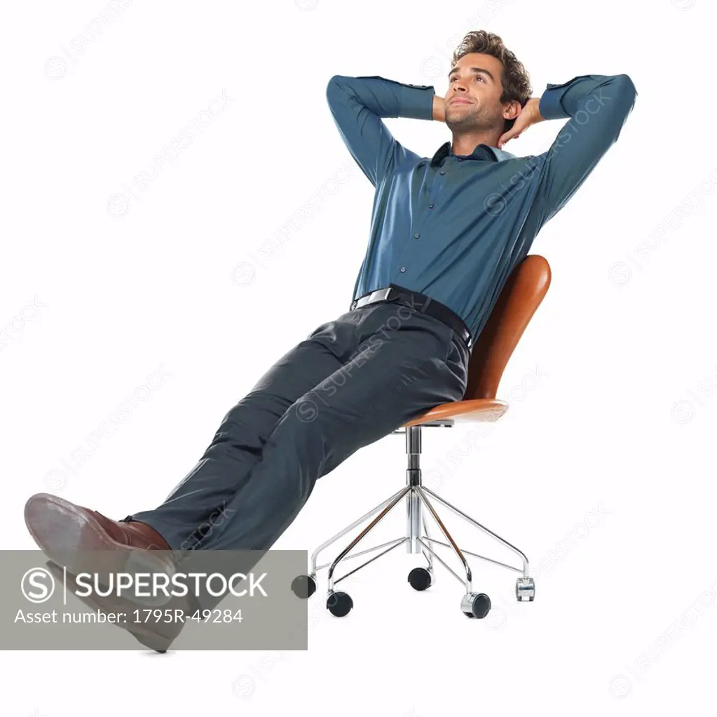 Studio shot of young business man relaxing on chair with hands behind head