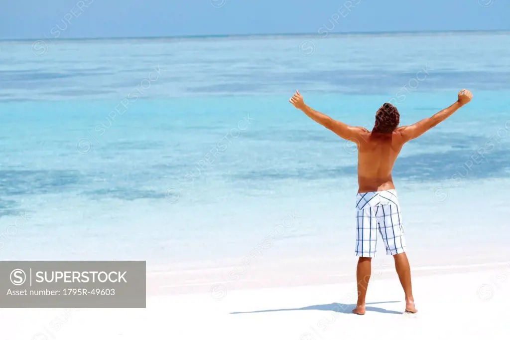 Man standing with his arms wide open on beach