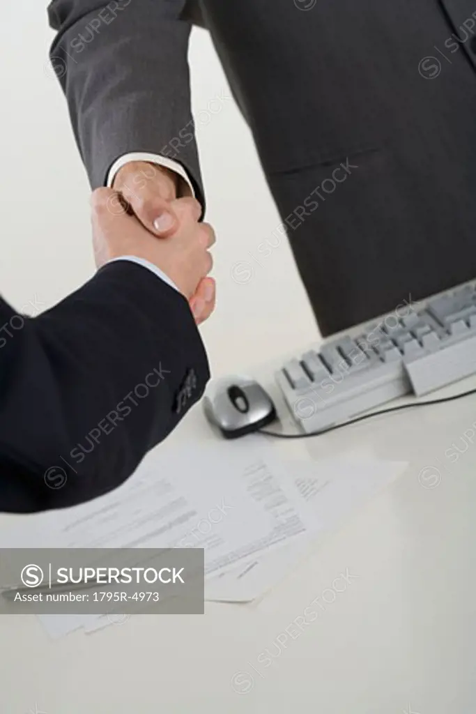 Businessmen shaking hands over computer