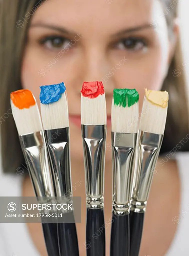Paintbrushes with paint in front of woman's face