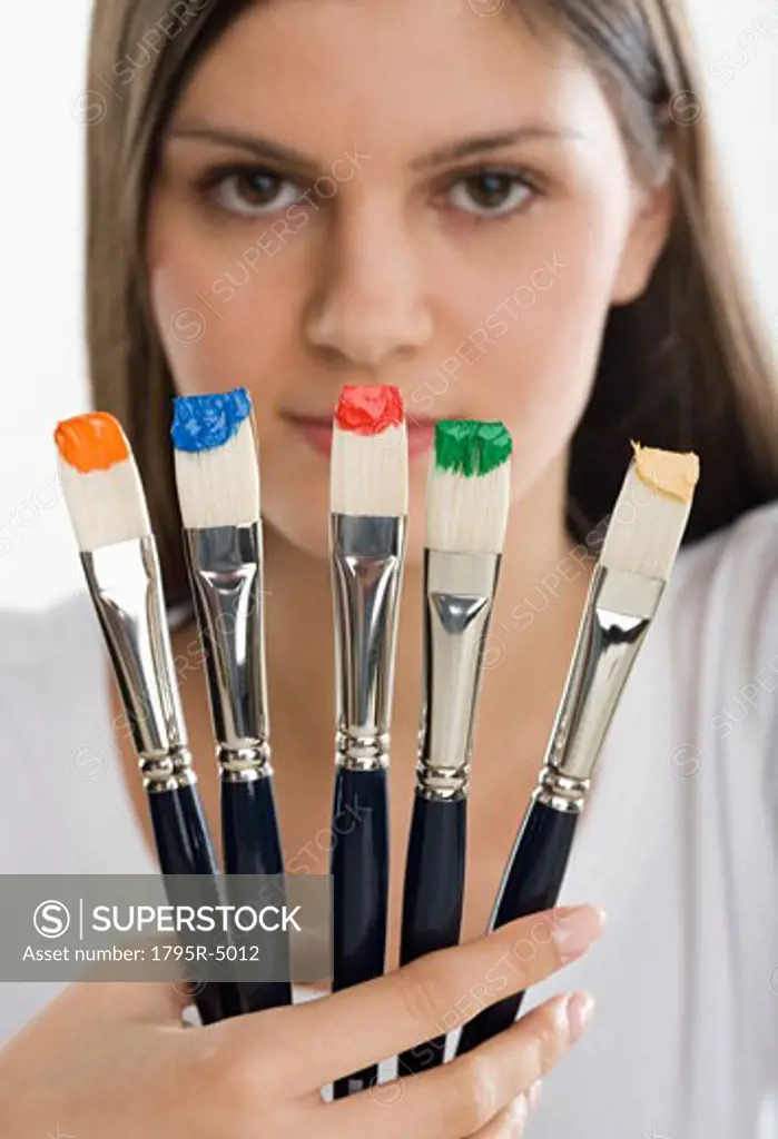 Paintbrushes with paint in front of woman's face
