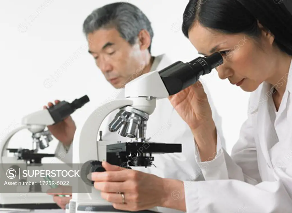 Man and woman in lab coats using microscopes