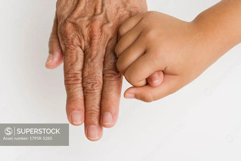 Close-up of child's hand holding pinky finger on senior's hand