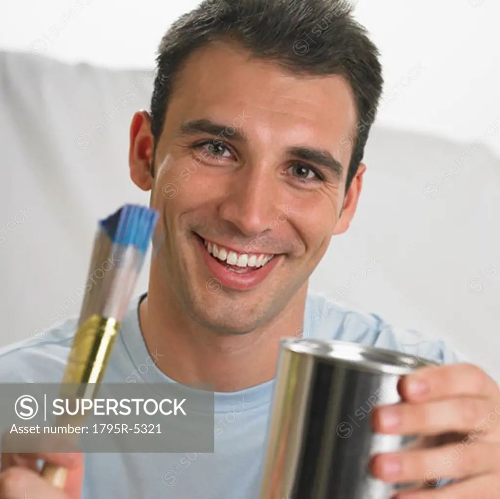 Man smiling and holding paintbrush and paint can