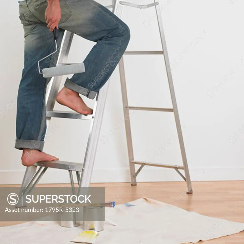 Man walking up ladder with paint roller indoors