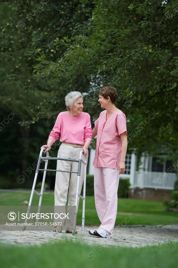 Senior woman walking with walker with help of nursing assistant