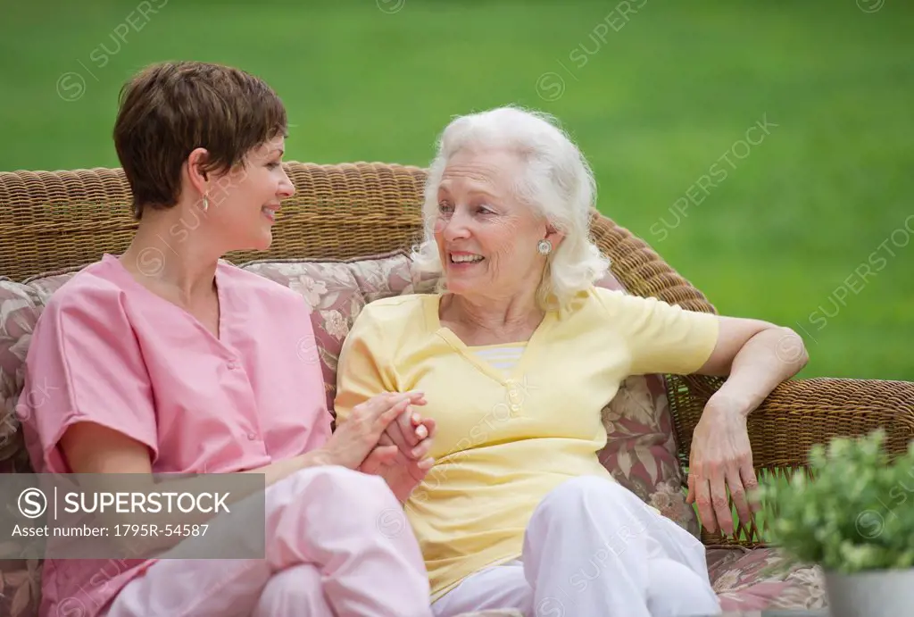 Senior woman and nursing assistant relaxing on outdoor sofa