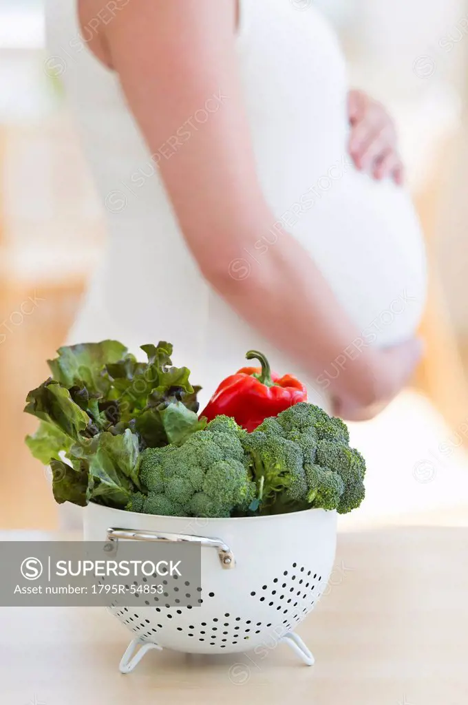 Fresh vegetables in colander, pregnant woman in background