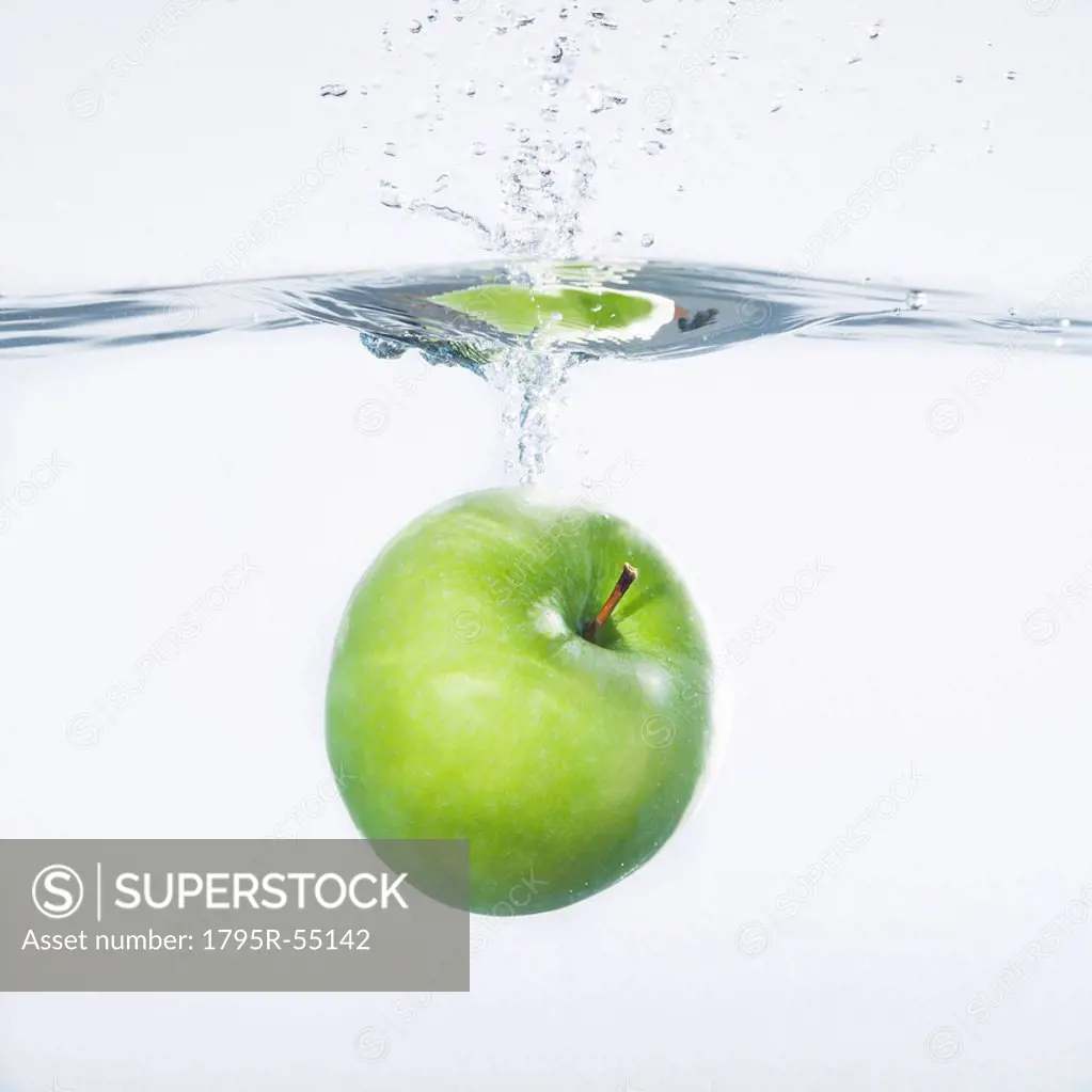 Green apple splashing into water, studio shot
