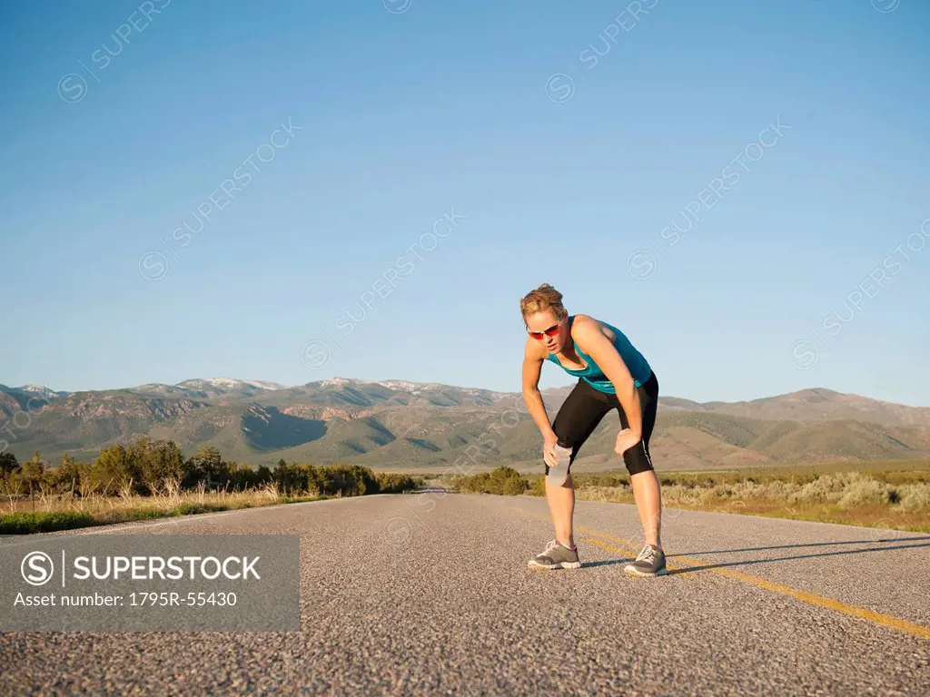 USA, Utah, Kanosh, Mid adult woman taking break from running on empty road