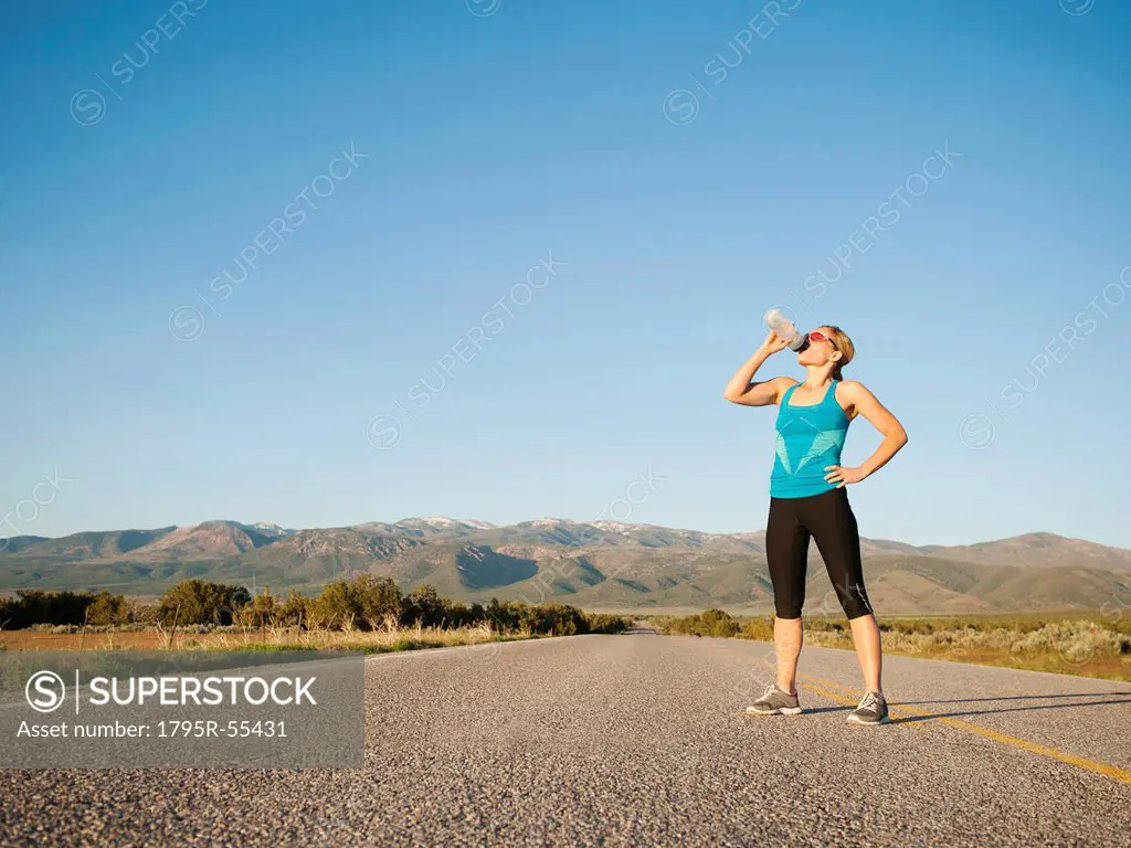 Mid adult woman drinking water while taking break from running on empty road