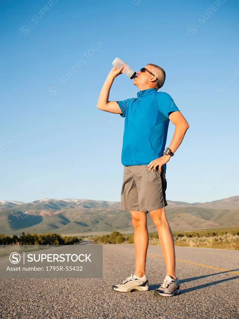 Mid adult an drinking water while taking break from running on empty road