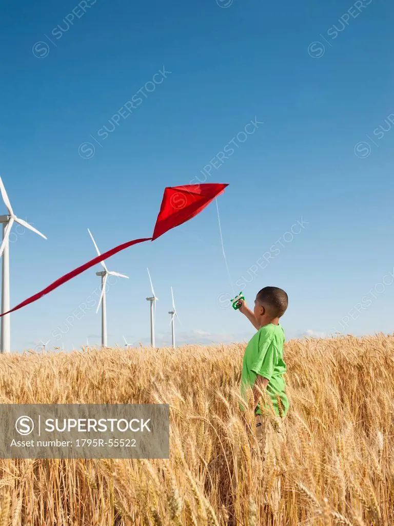 USA, Oregon, Wasco, Boy 8_9 playing with kite in wheat field, wind turbines in background