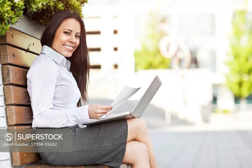 Portrait of young businesswoman sitting on bench using laptop