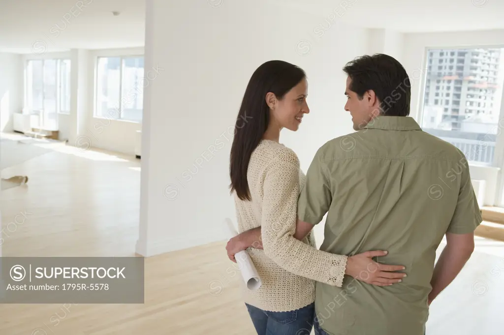 Couple hugging and holding blueprints in empty house