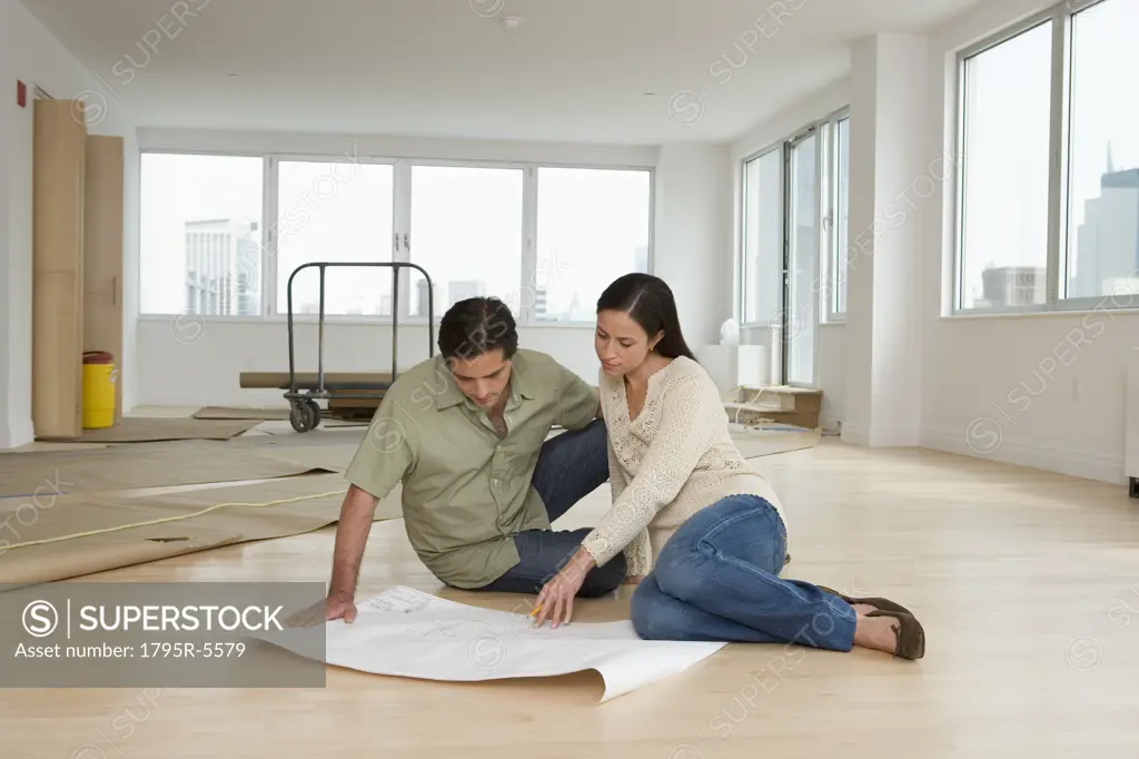 Couple looking at blueprints on floor in new house