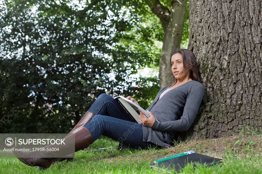 Young woman sitting under tree reading books