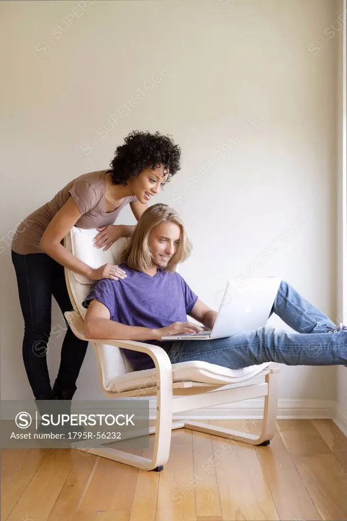 Young woman looking at man using laptop at home