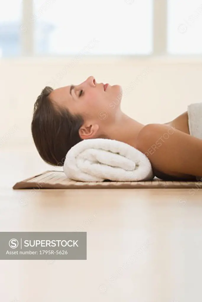 Woman laying on mat with rolled towel under neck