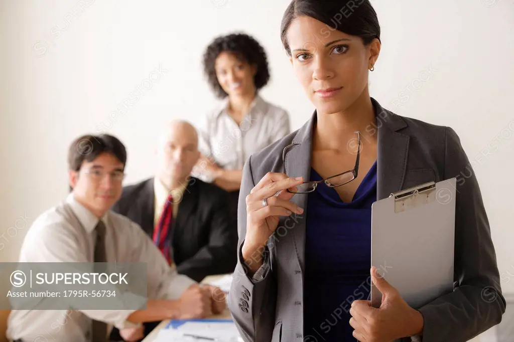 Young businesswoman looking at camera, business team in background