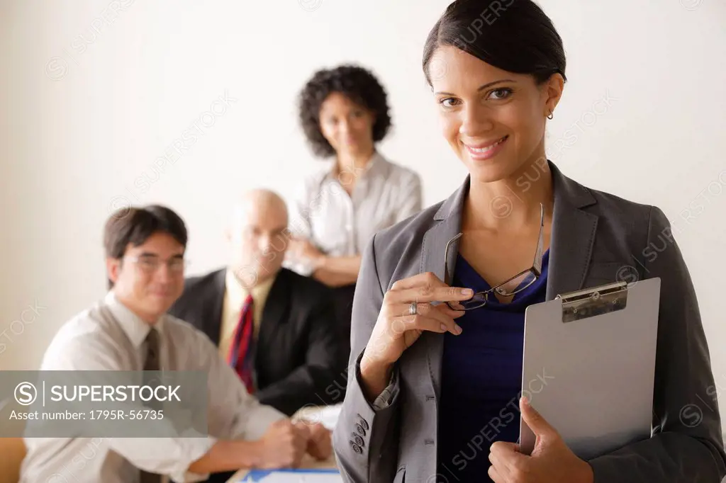 Young businesswoman looking at camera, business team in background