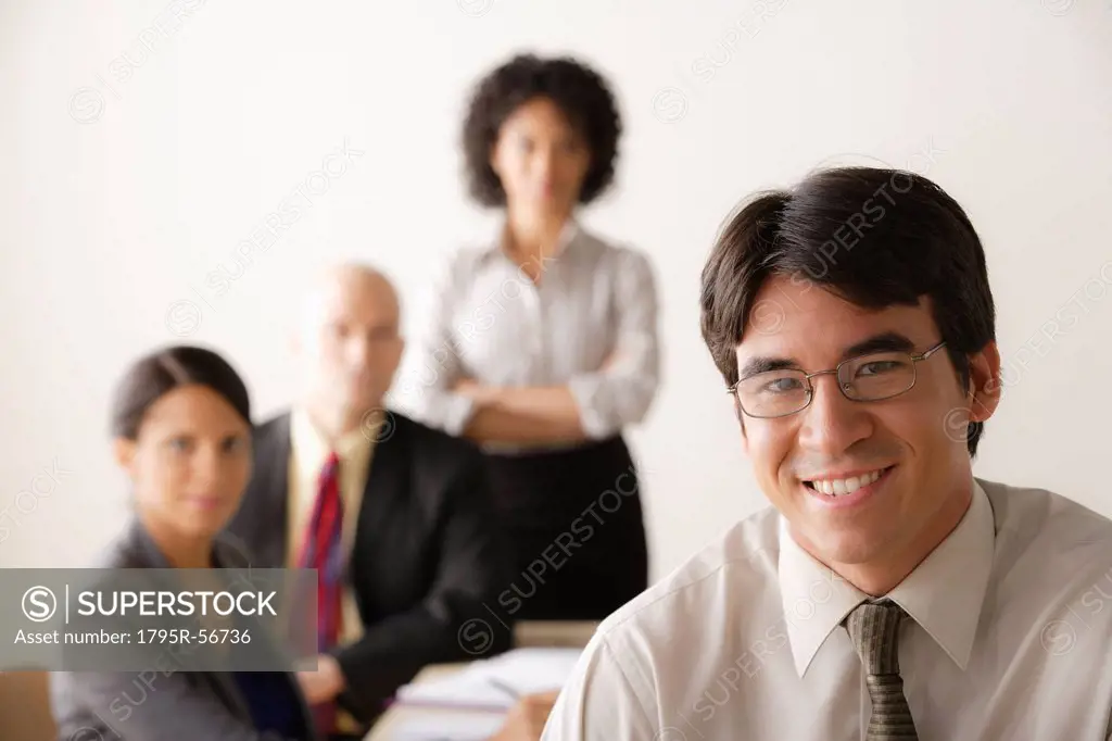 Young businessman looking at camera, business team in background