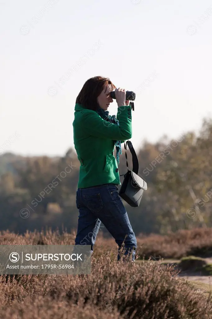 The Netherlands, Veluwezoom, Posbank, Woman in countryside looking through binoculars