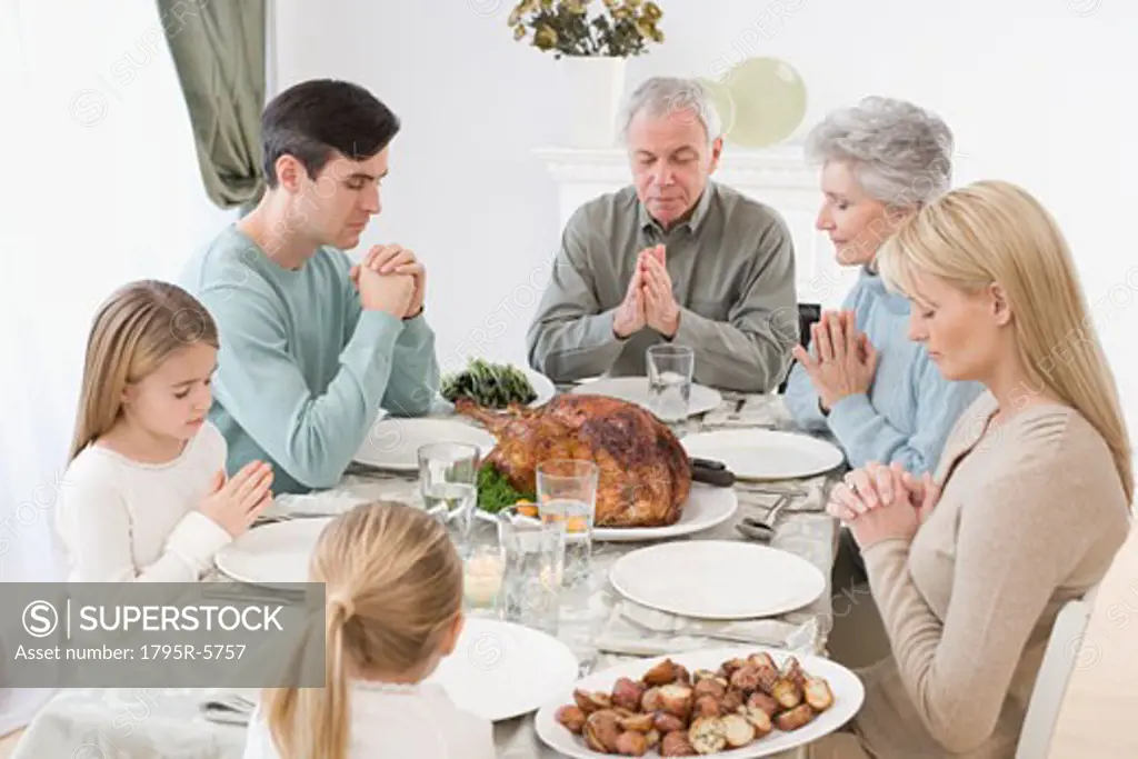 Family saying grace at Thanksgiving table