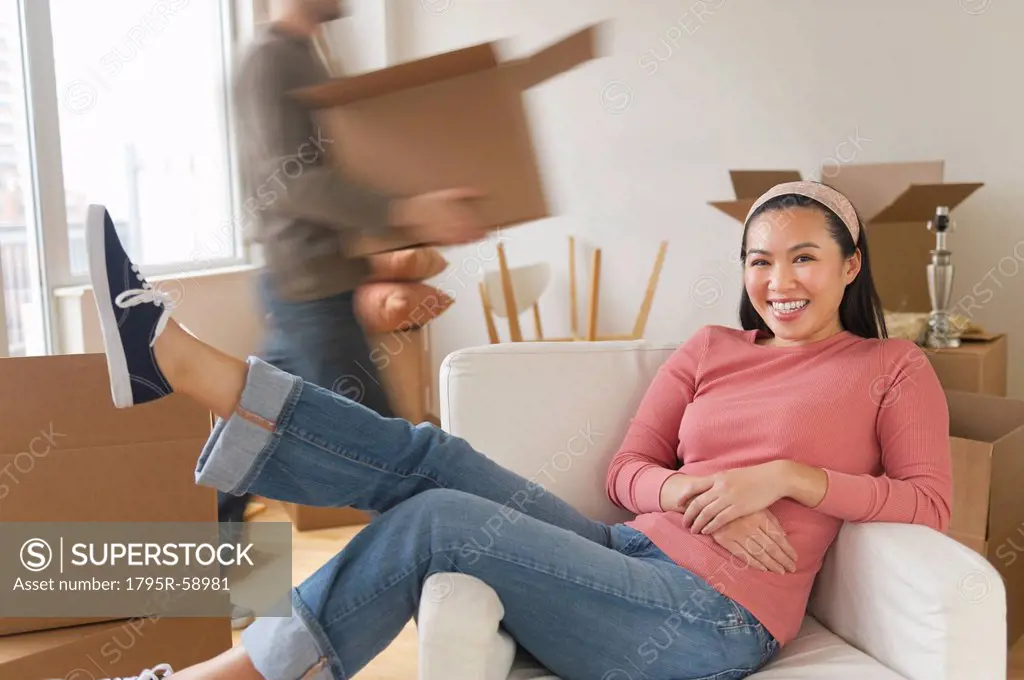 Man carrying boxes, woman resting in chair at new home