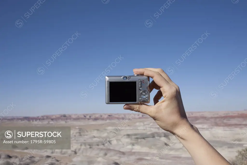 Hand of woman holding camera up against blue sky