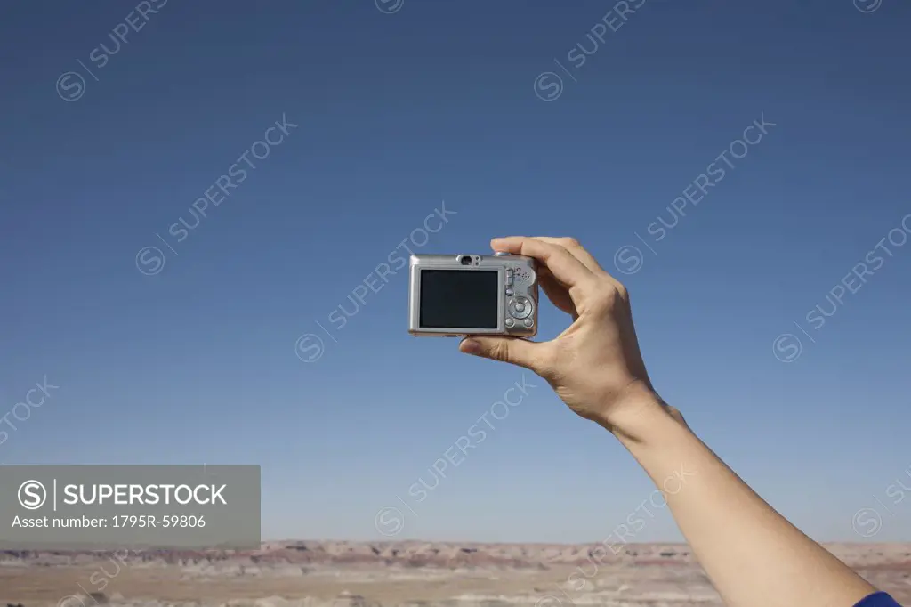 Hand of woman holding camera up against blue sky