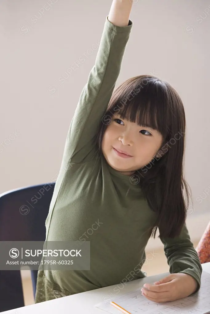 Girl (6-7) raising hand in classroom