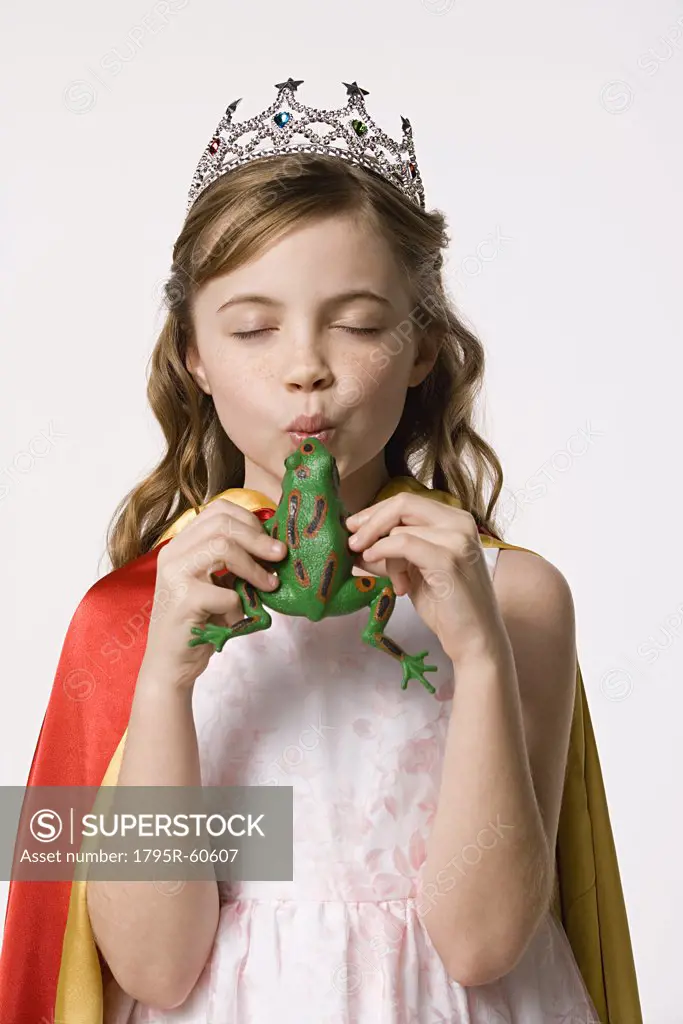 Studio portrait of girl (8-9) wearing princess costume and kissing toy frog