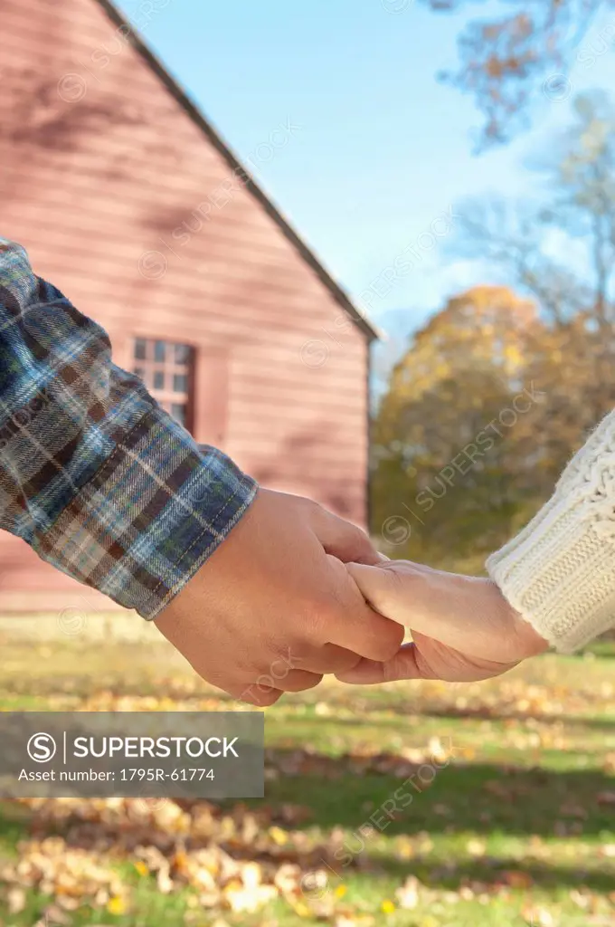 Close_up of couple holding hands in front of cottage house