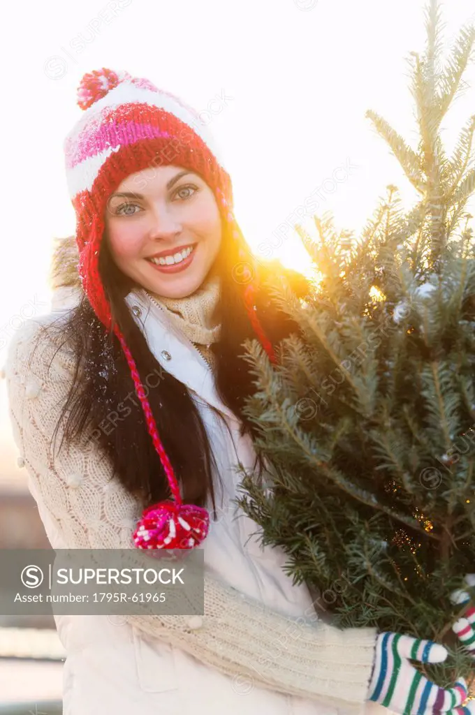 Portrait of young woman carrying Christms tree