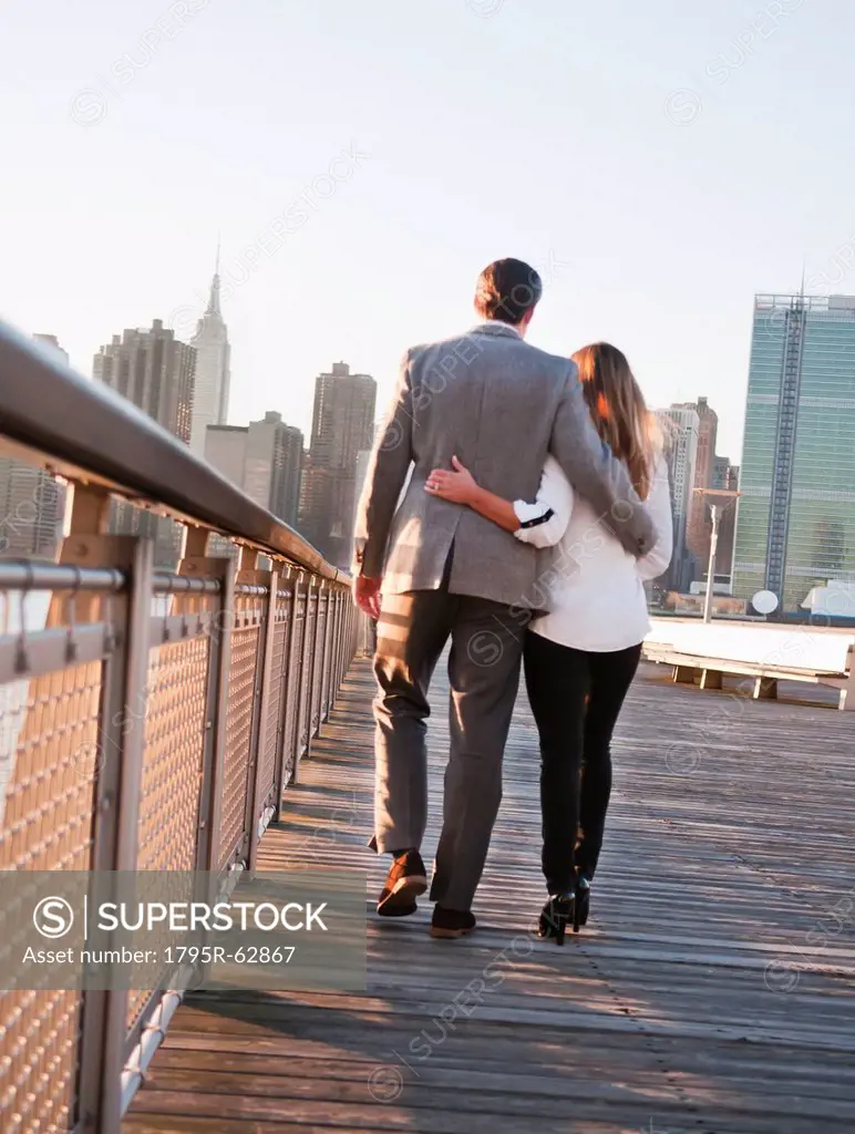 USA, New York, Long Island City, Rear view of young couple walking on boardwalk, Manhattan skyline in background