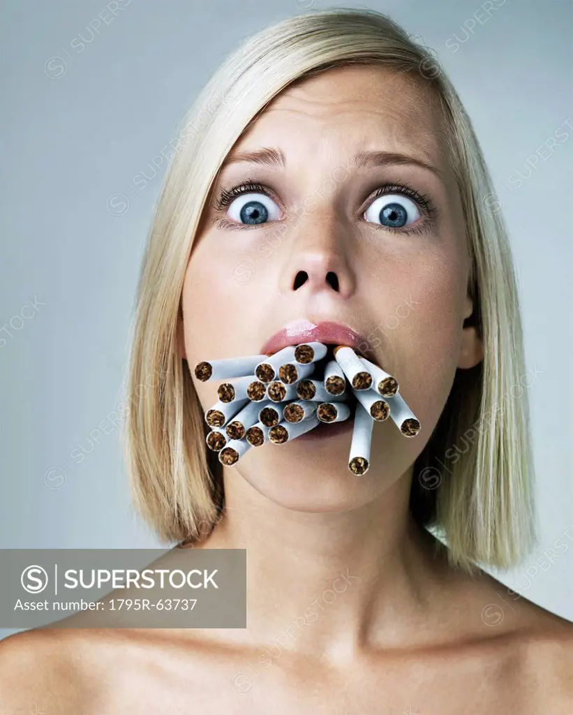 Young woman looking alarmed with mouthful of cigarettes, studio shot