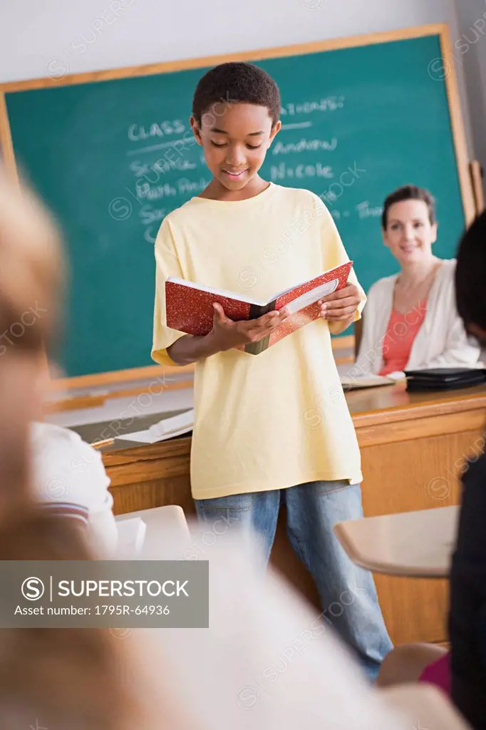 Boy reading from book in front of class