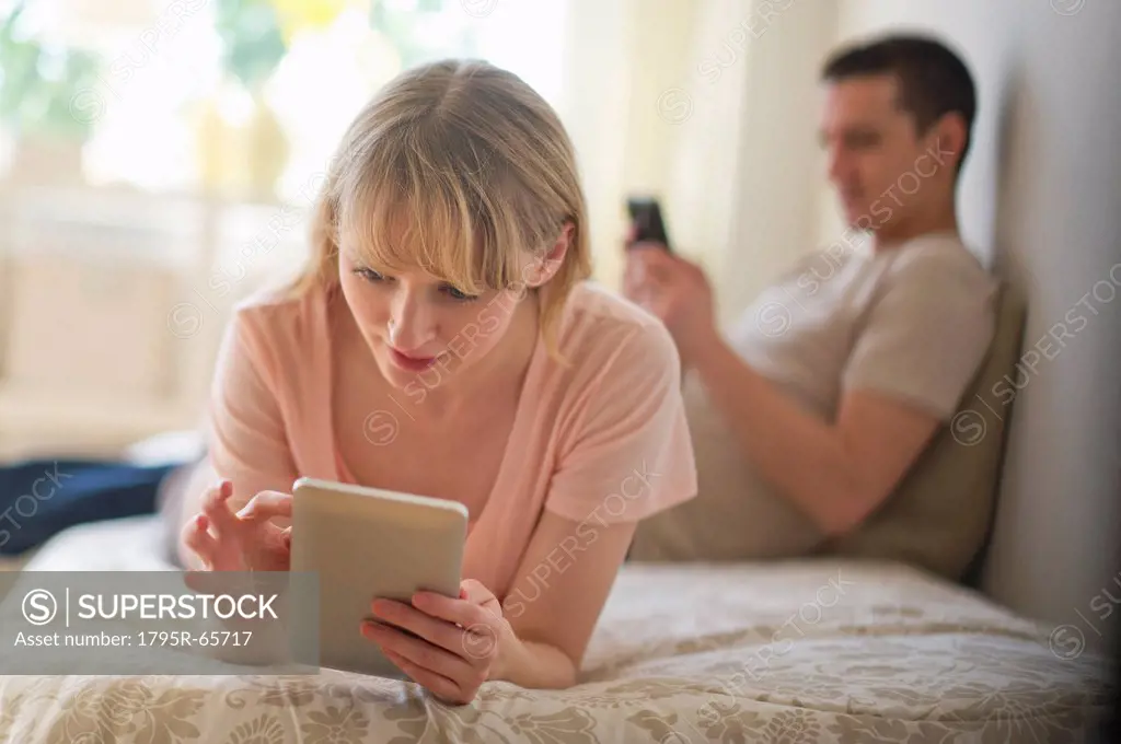 Couple lying on bed and using digital devices