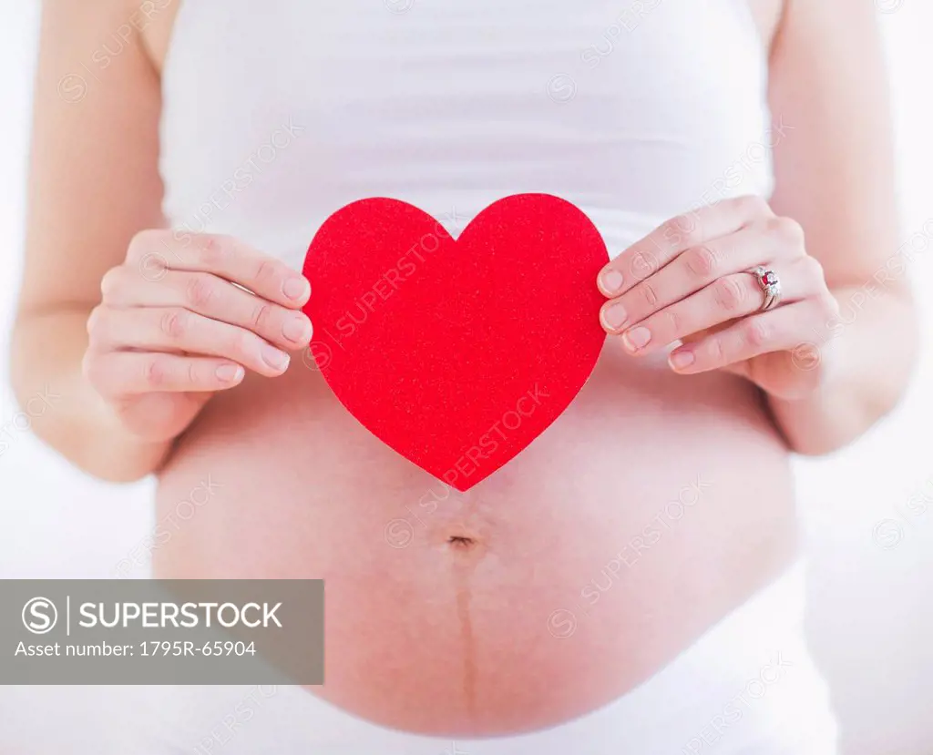 Pregnant woman holding red paper heart on her belly