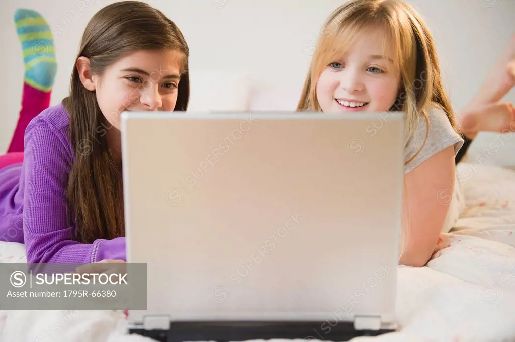Two girls using laptop on bed
